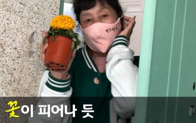 [사진1] '꽃이 피어나 듯 나눔의 마음이 피어나다.'라는 문구와 함께 현관에서 꽃을 들고 있는 여자의 모습이 담긴 사진